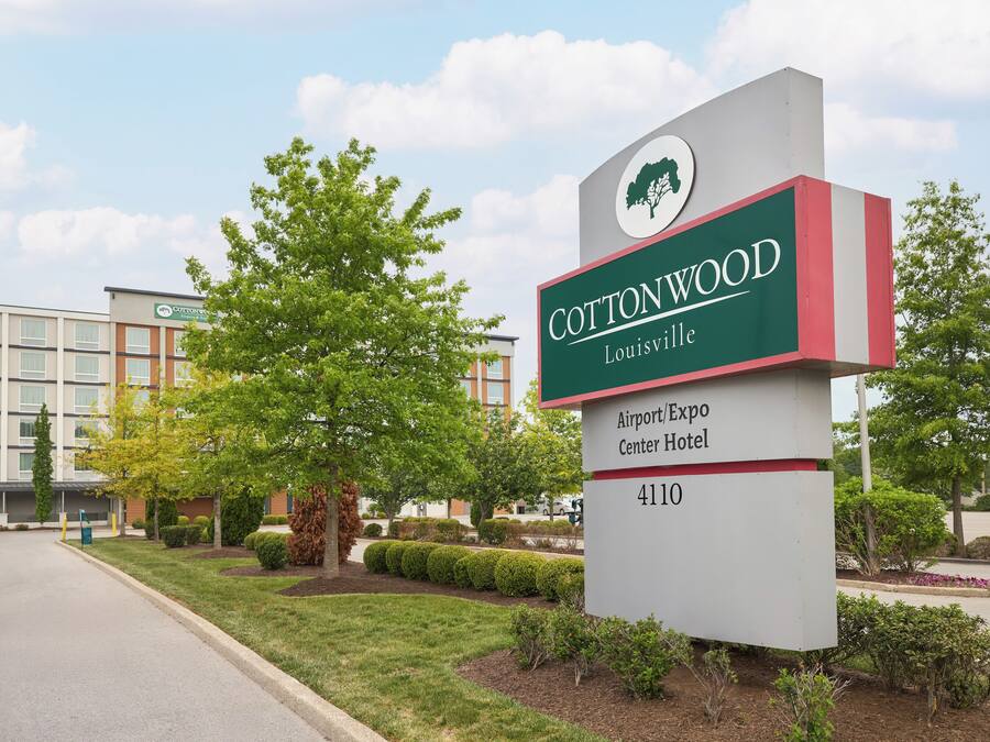 Schild für das Cottonwood Louisville Airport/Expo Center Hotel mit einem modernen Gebäude im Hintergrund.
