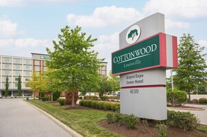 Señal del hotel Cottonwood Louisville Airport/Expo Center con un edificio moderno al fondo.