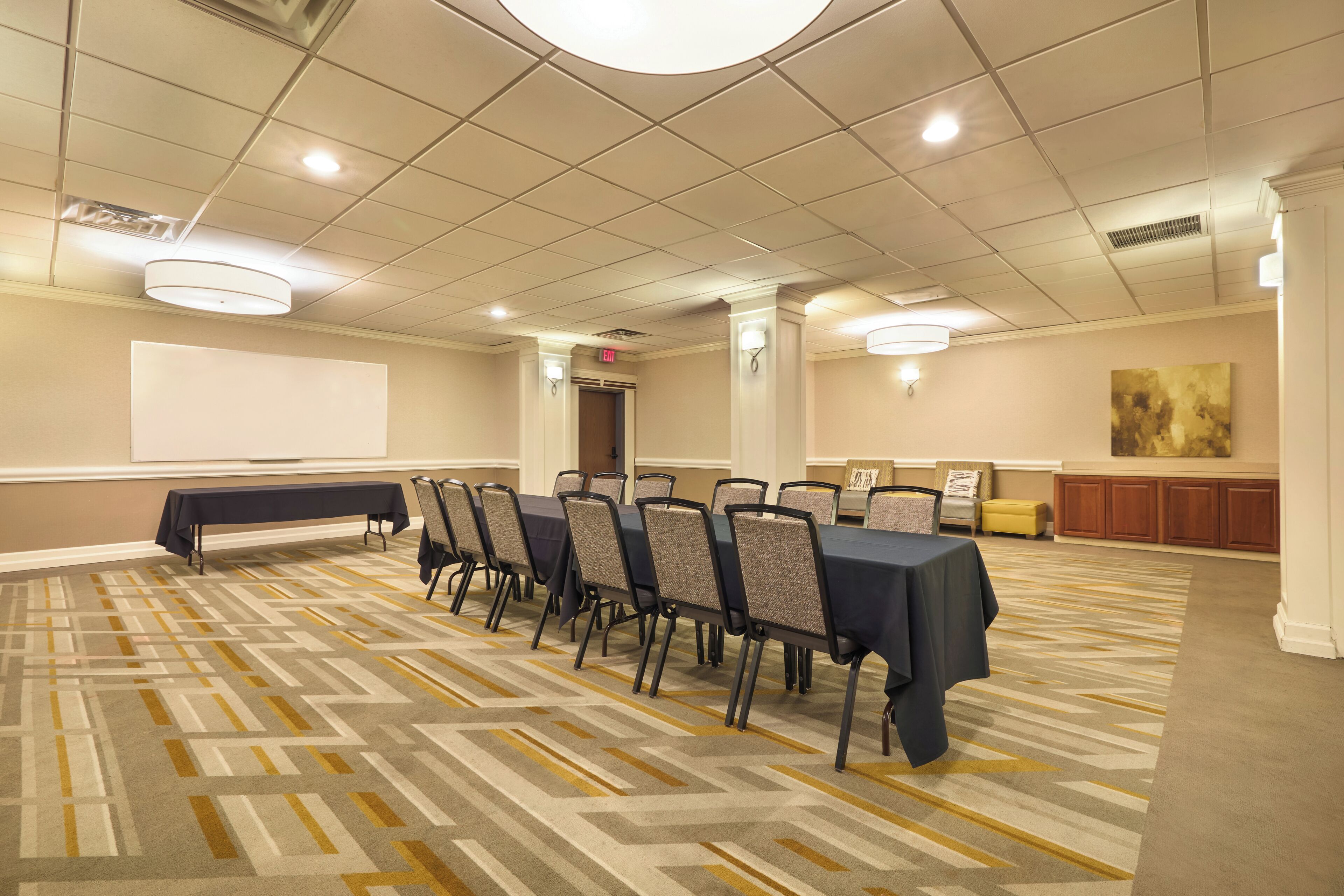 Un salón de conferencias con una larga mesa, sillas, una pantalla de proyector y piso alfombrado.