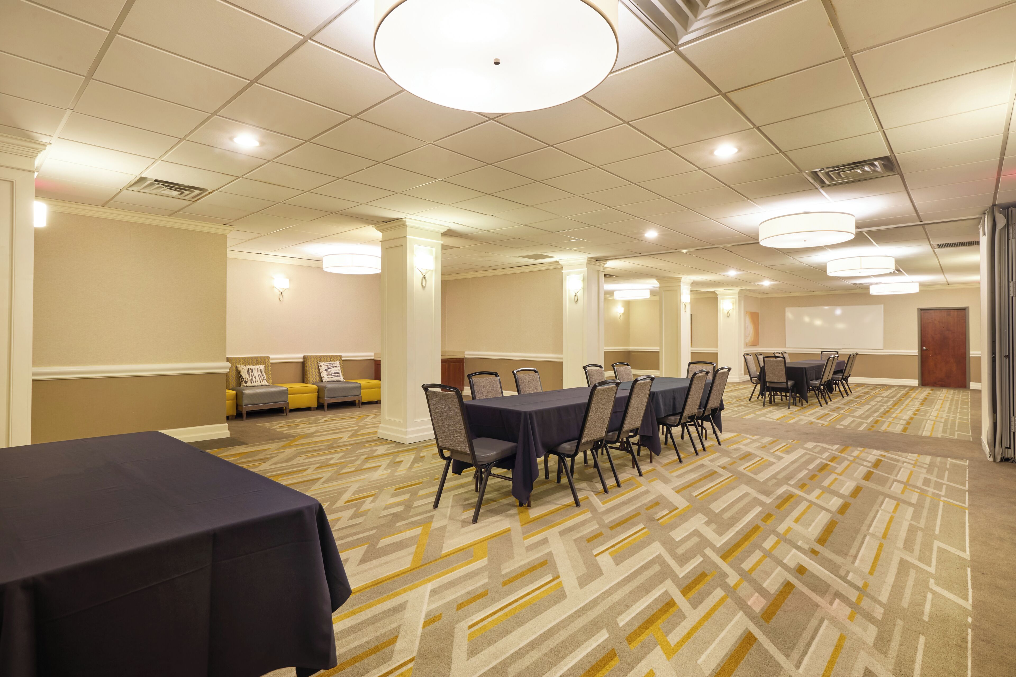 A conference room with tables and chairs, a patterned carpet, and a whiteboard on the wall.