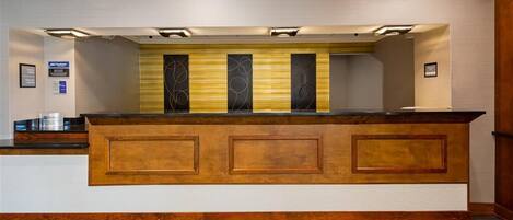 A reception desk with a wooden finish, a light-colored wall, and a framed sign on the left.