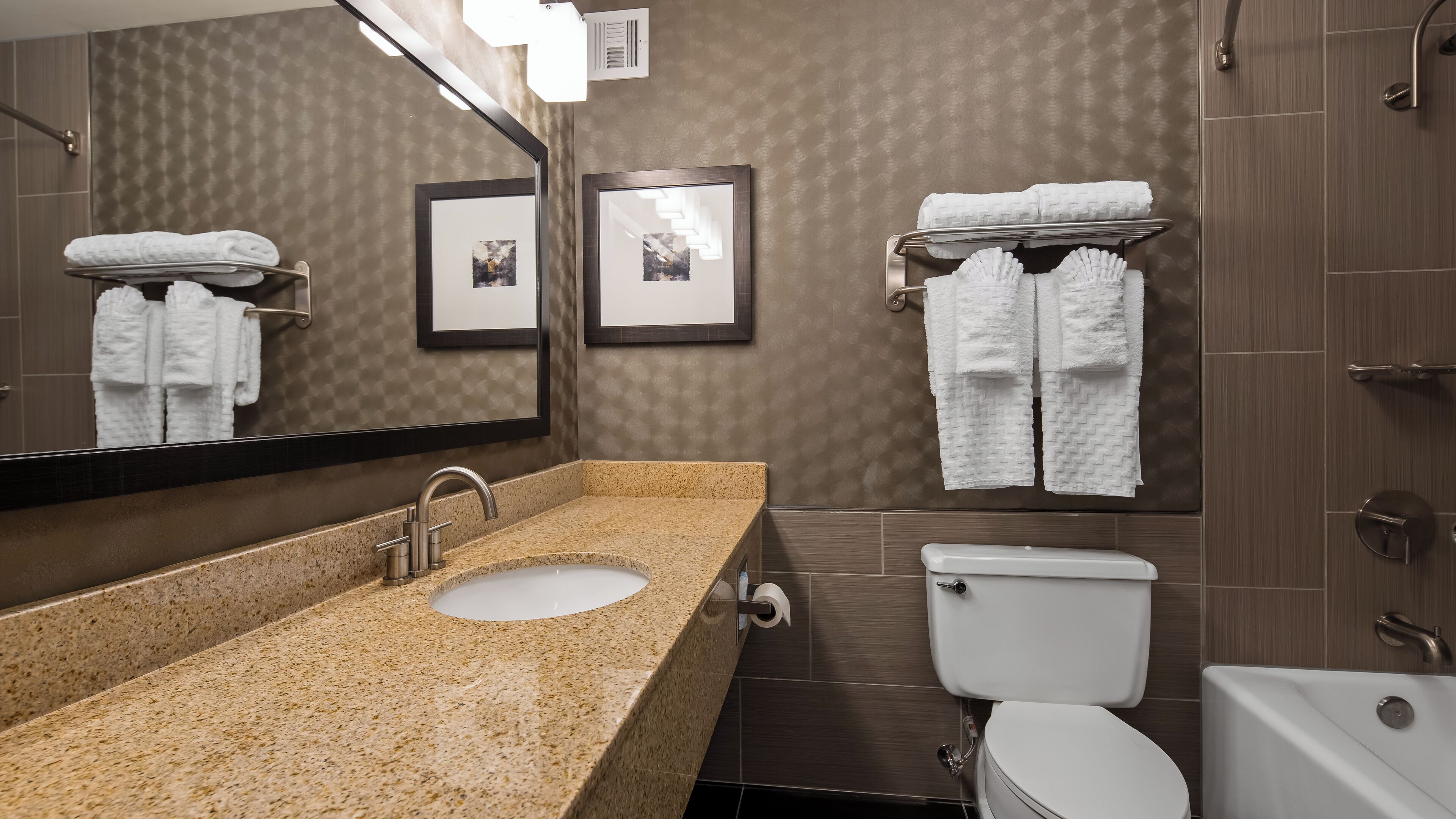 Un baño moderno con lavamanos de granito, un espejo, un inodoro y una bañera.