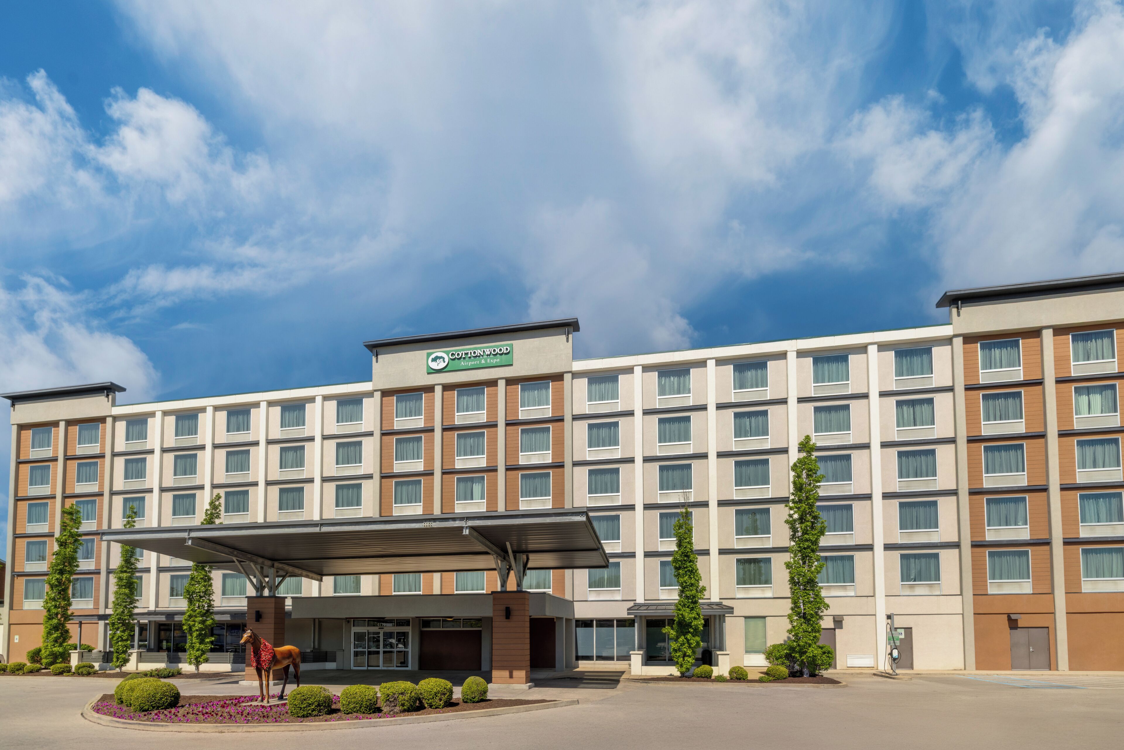 A multi-story hotel with a flat facade, a covered entrance, and a sign indicating it is a Cottonwood Airport & Expo hotel.