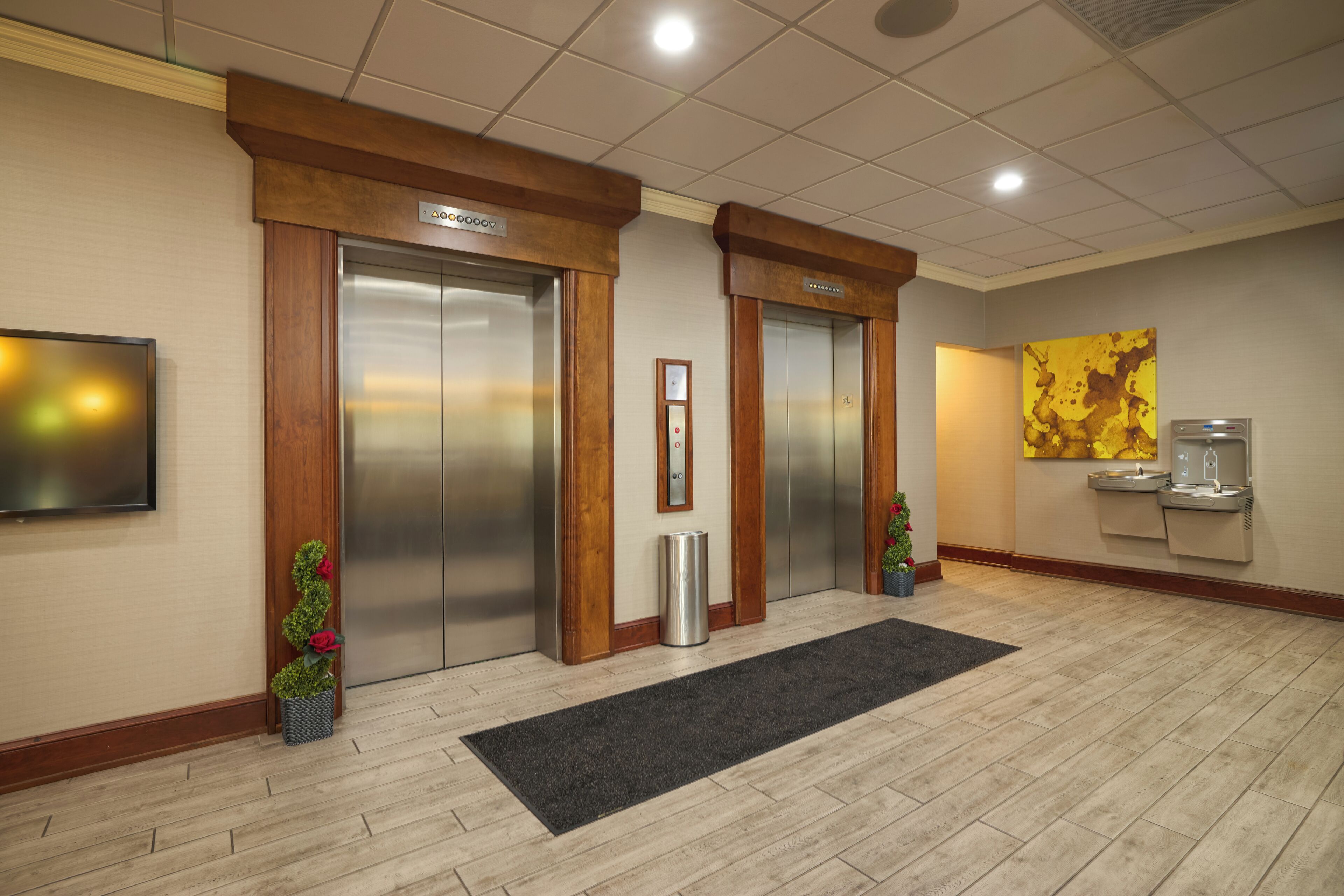 A hotel lobby with two elevators, a water dispenser, and a television on the wall.