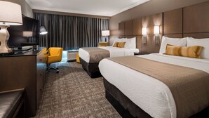 A hotel room with two beds, a desk with a computer, a chair, and a large window with curtains.