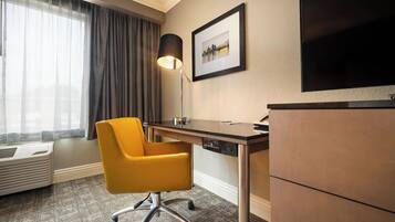 A hotel room with a desk, chair, lamp, and a flat-screen TV.