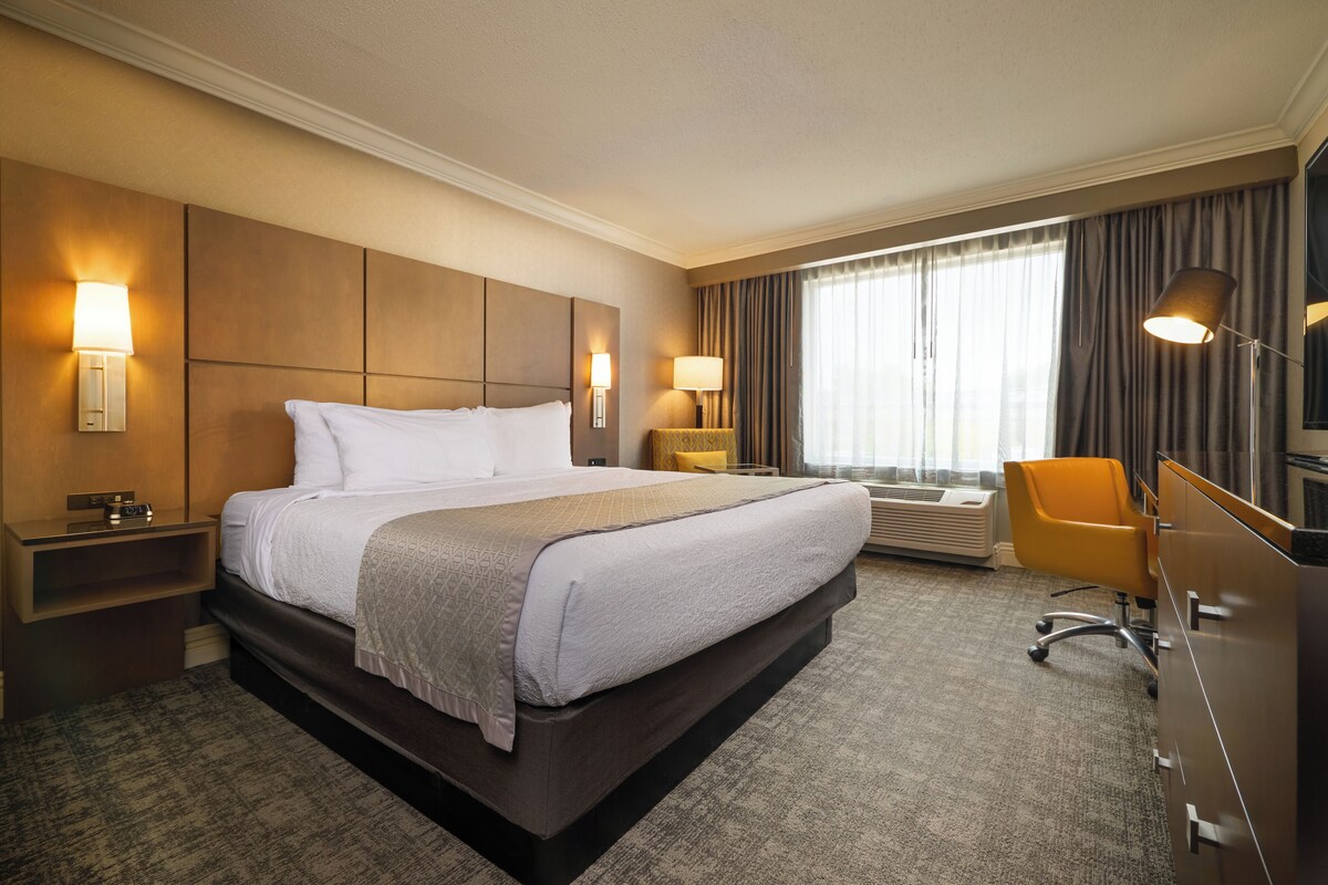 Quarto de hotel com uma cama grande, abajures, escrivaninha e uma cadeira.