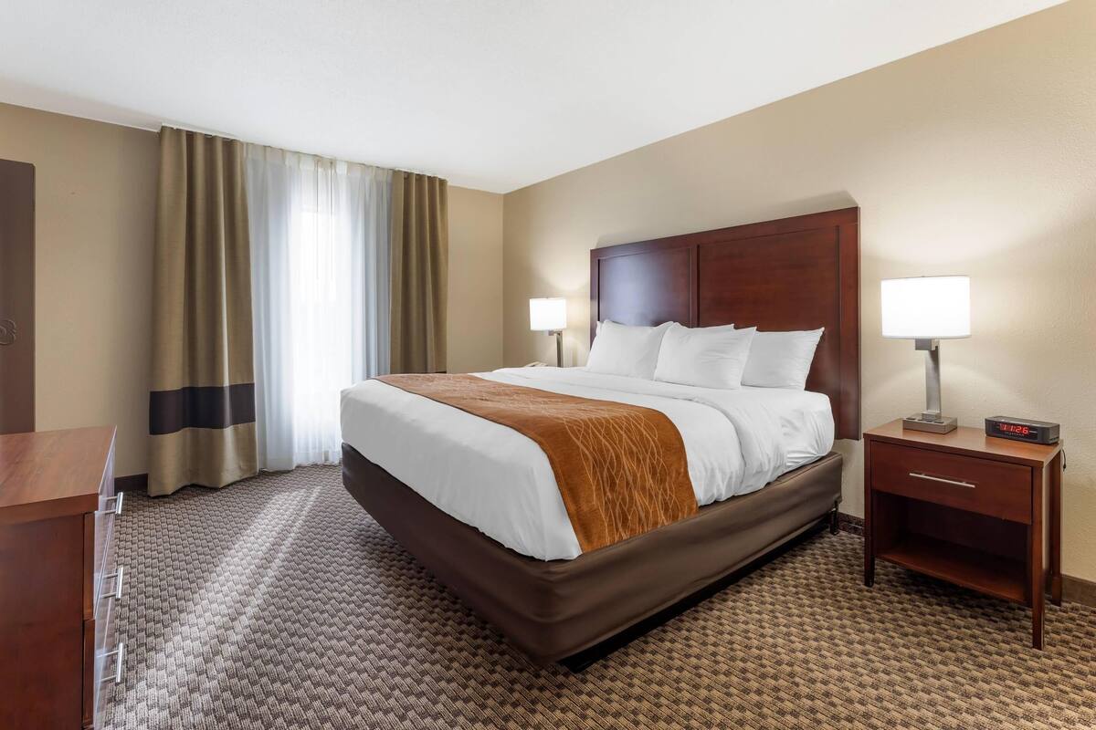 A hotel room with a large bed, bedside lamps, a wooden nightstand, and a carpeted floor.