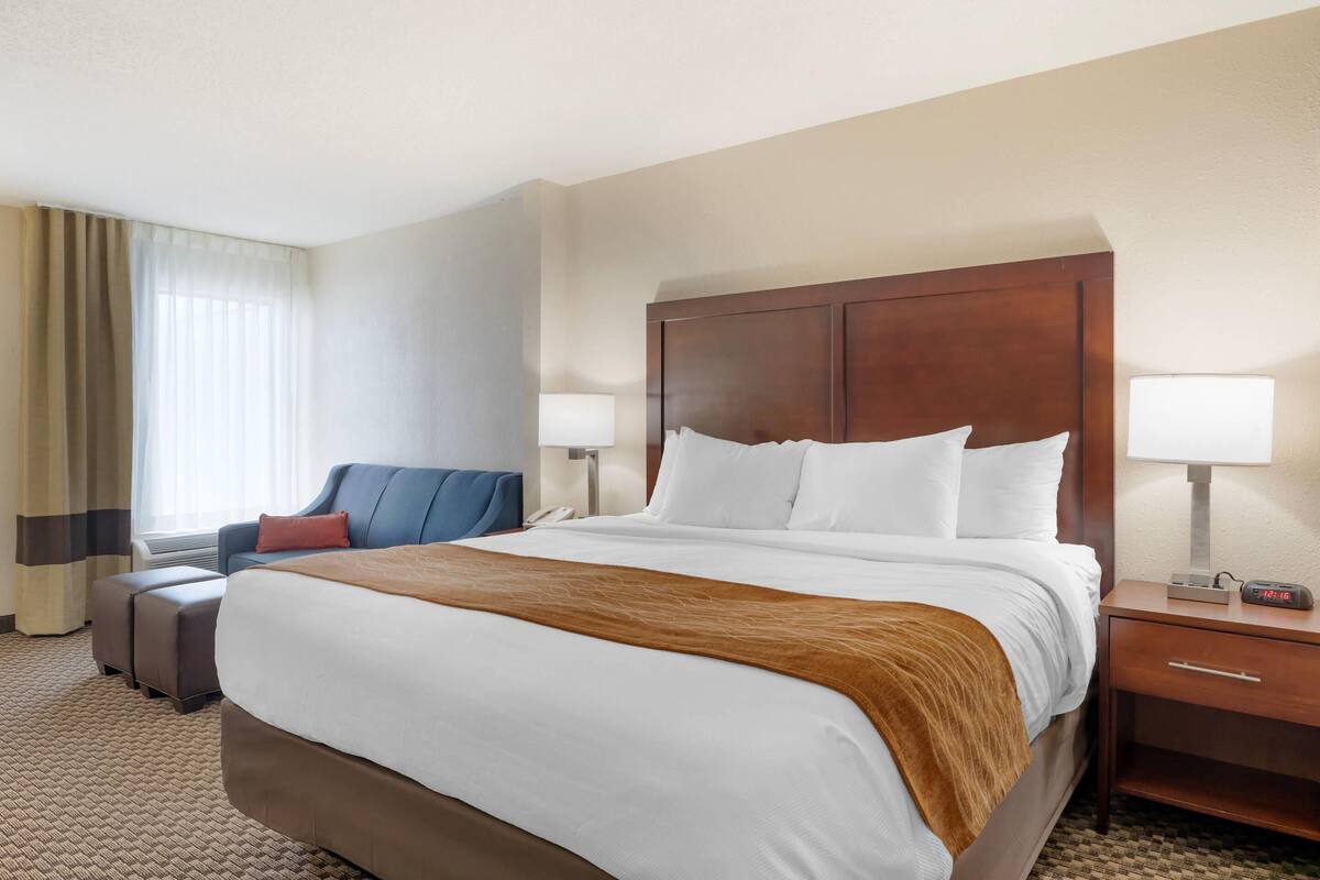 A hotel room with a large bed, a desk, a chair, and a lamp.
