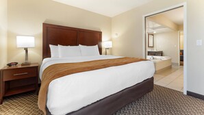 A hotel room with a large bed, two bedside tables with lamps, a bathroom visible through an open door, and a carpeted floor. - Comfort Inn Ebensburg (Ebensburg)