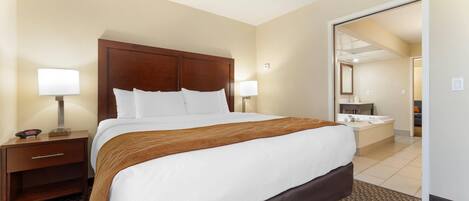 A hotel room with a large bed, two bedside tables with lamps, a bathroom visible through an open door, and a carpeted floor.