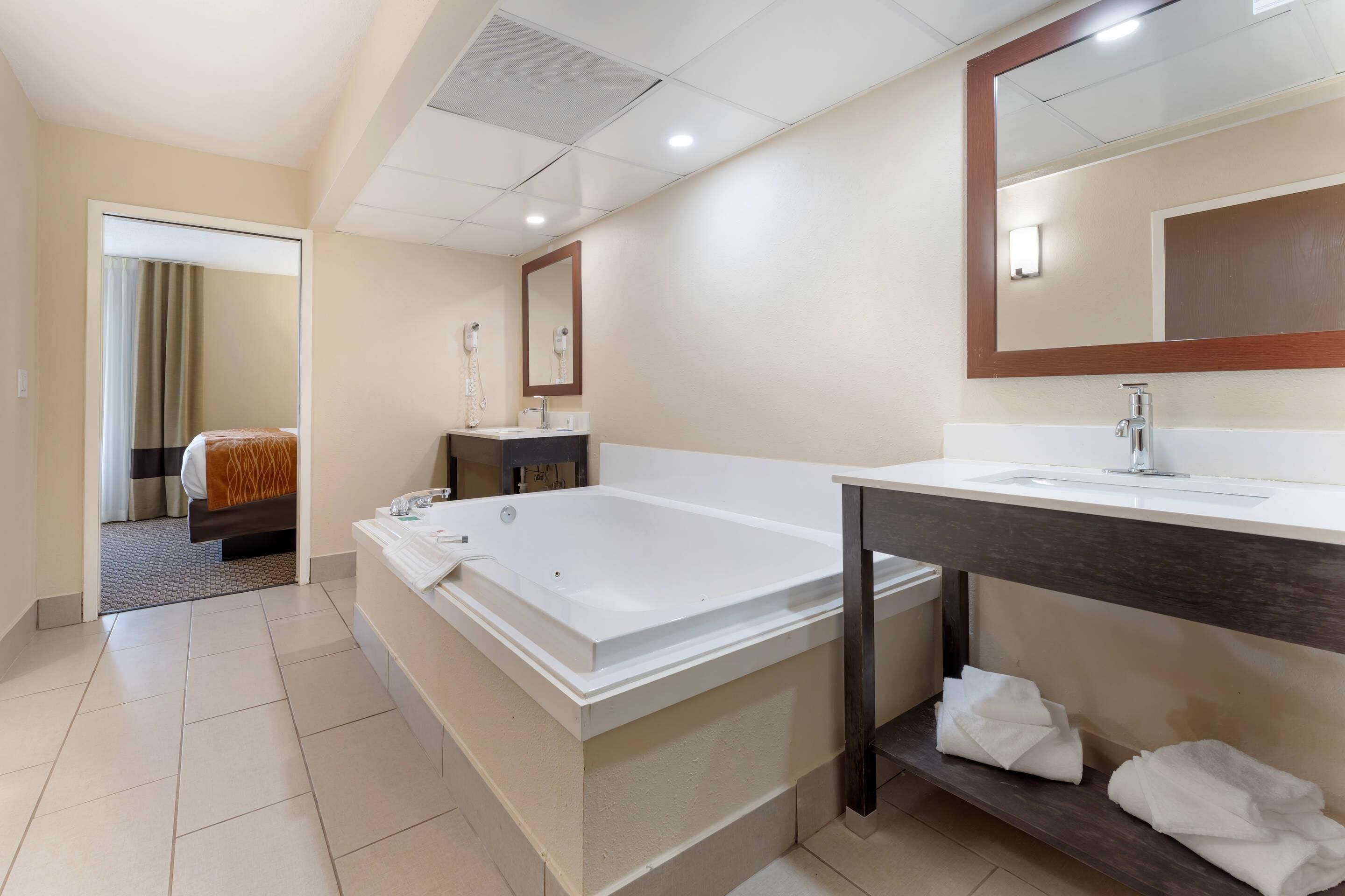 Ein Hotelbad mit einer großen Wanne, einem Waschbecken, einem Spiegel und einer Dusche.
