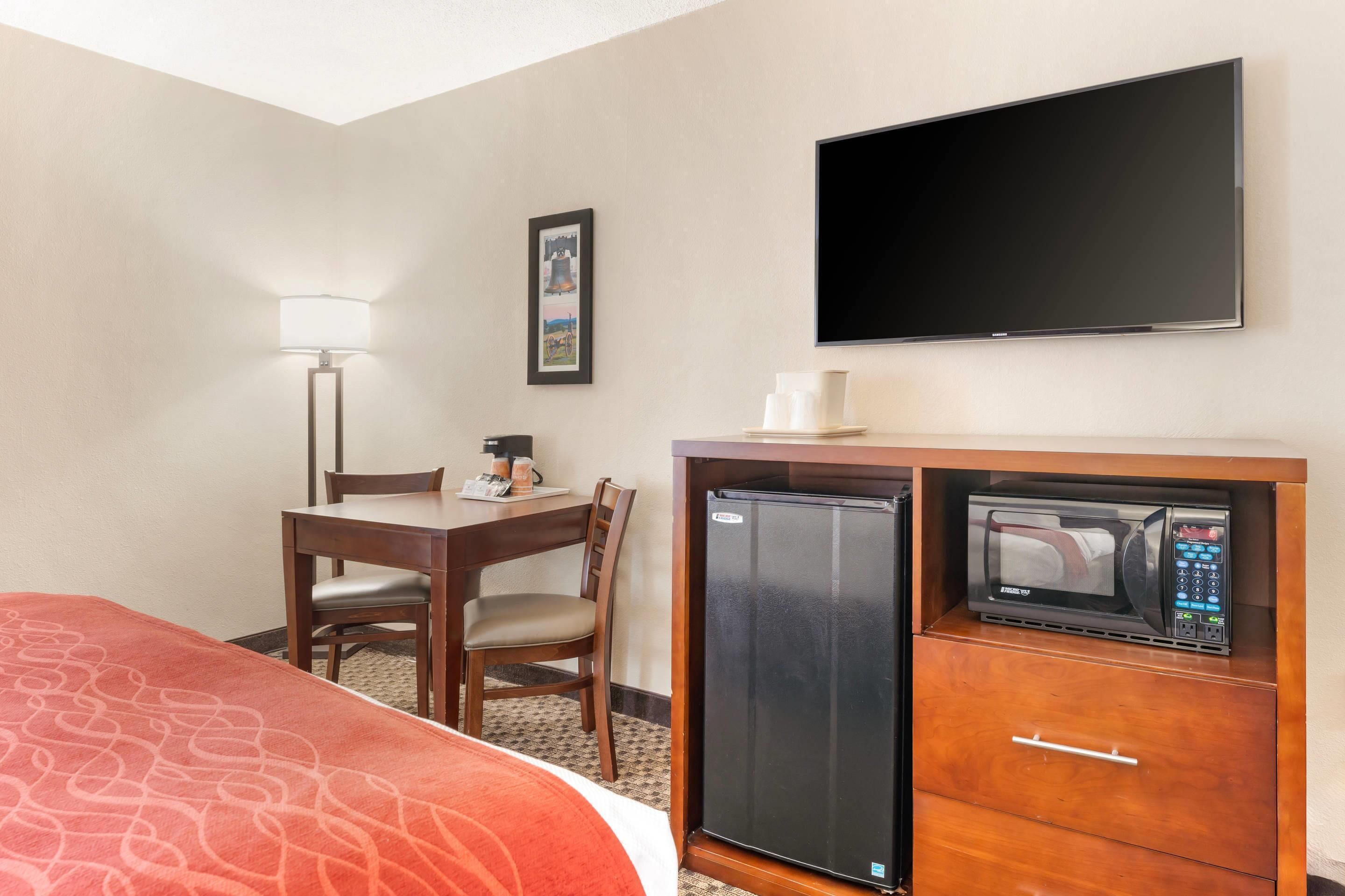 A hotel room with a bed, a desk with a chair, a refrigerator with a microwave, a flat-screen TV, and a wall-mounted picture.