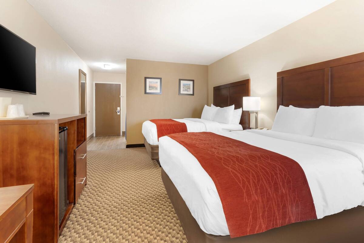 A hotel room with two beds, a TV, a desk, and a door.