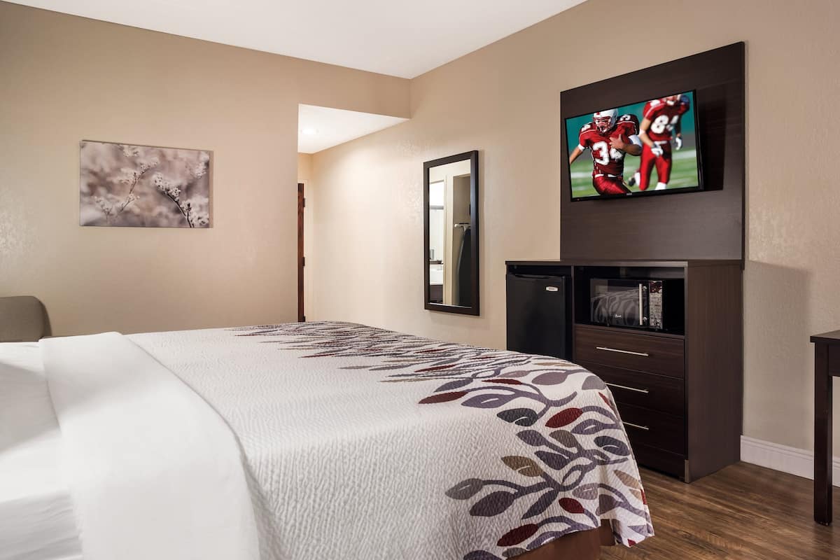 A hotel room with a large bed, a television mounted on the wall, a mirror, and a small cabinet.