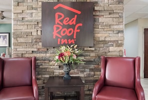 A Red Roof Inn sign on a stone wall, a vase with flowers on a table, and two leather chairs.