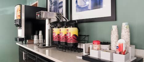 A coffee station with a coffee machine, disposable cups, and a coffee dispenser.