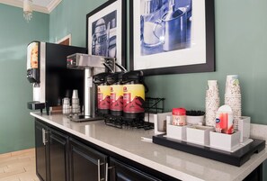 A coffee station with a coffee machine, disposable cups, and a coffee dispenser.