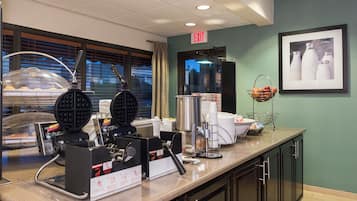 Un área de cocina en un hotel con máquinas para hacer gofres, una cafetera y un letrero que indica una salida.
