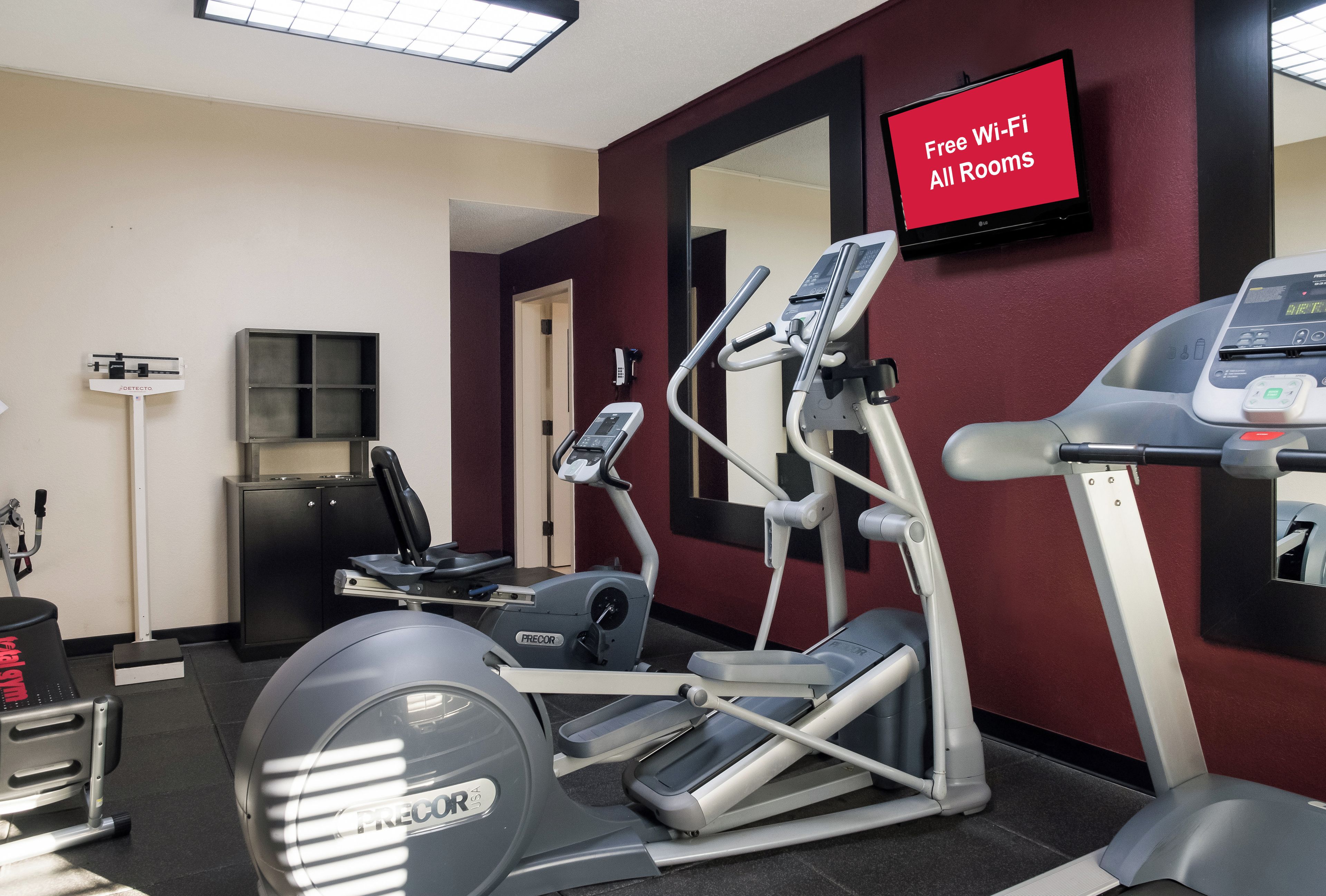 A gym with exercise equipment, a scale, and a TV displaying 'Free Wi-Fi All Rooms'.