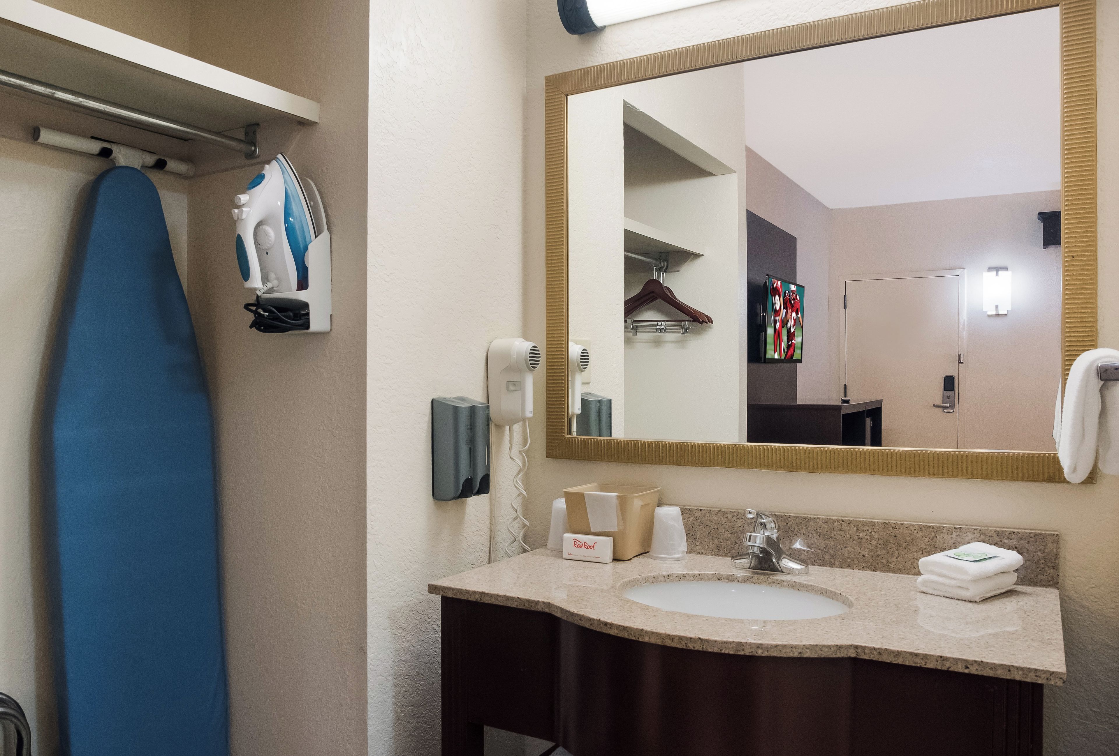 A bathroom with a sink, mirror, hanging clothes rack, and a blue ironing board.