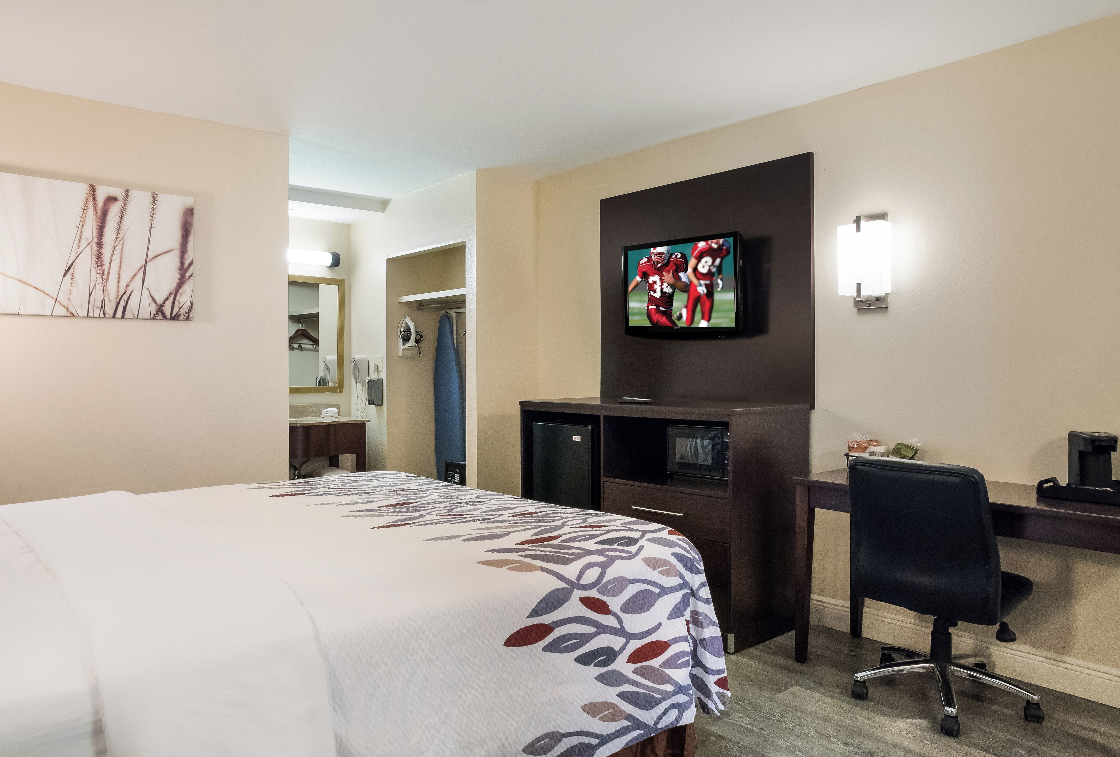 A hotel room with a bed, a desk, a television, and a mirror.
