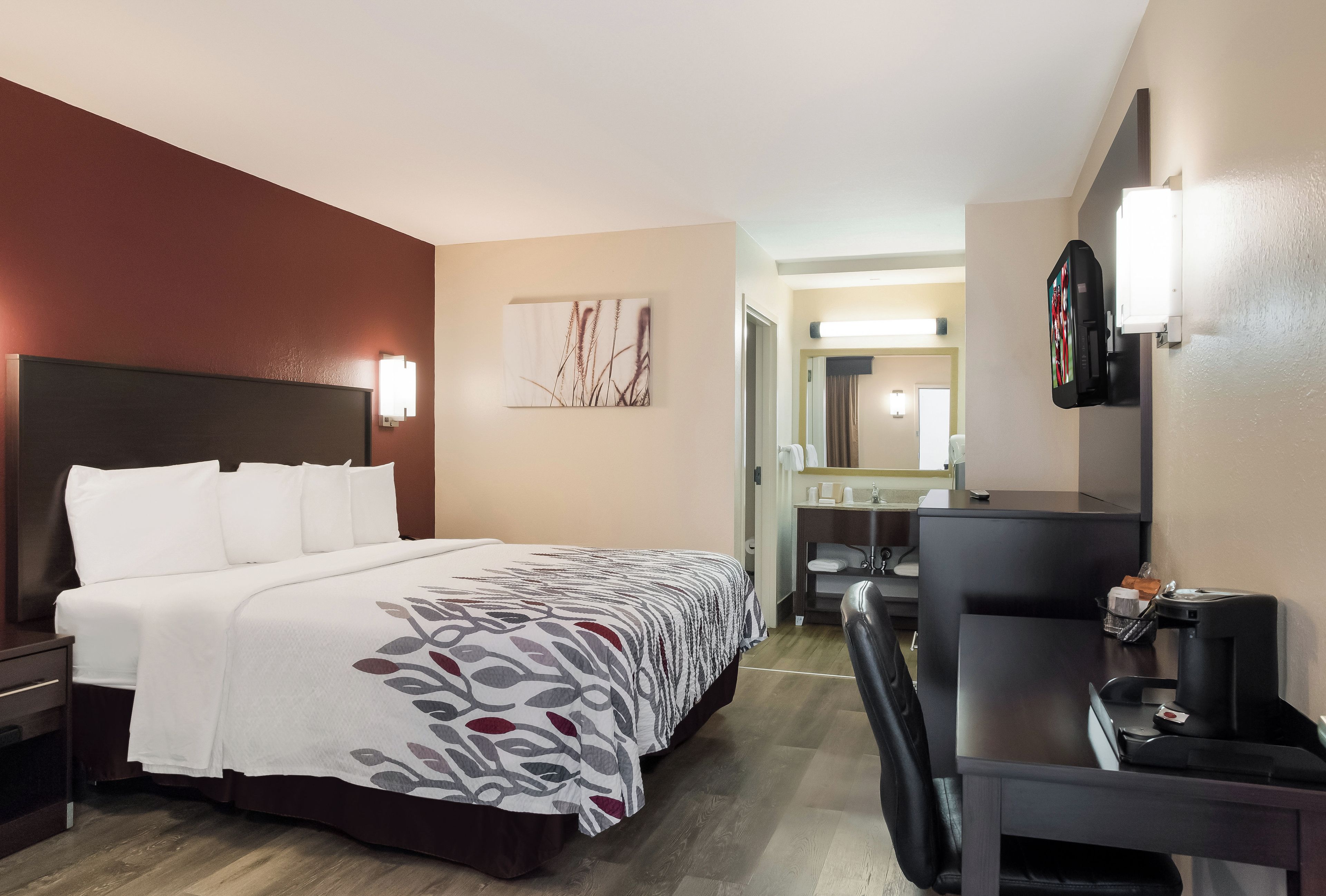 A hotel room with a bed, bedside table, desk, chair, and a television.