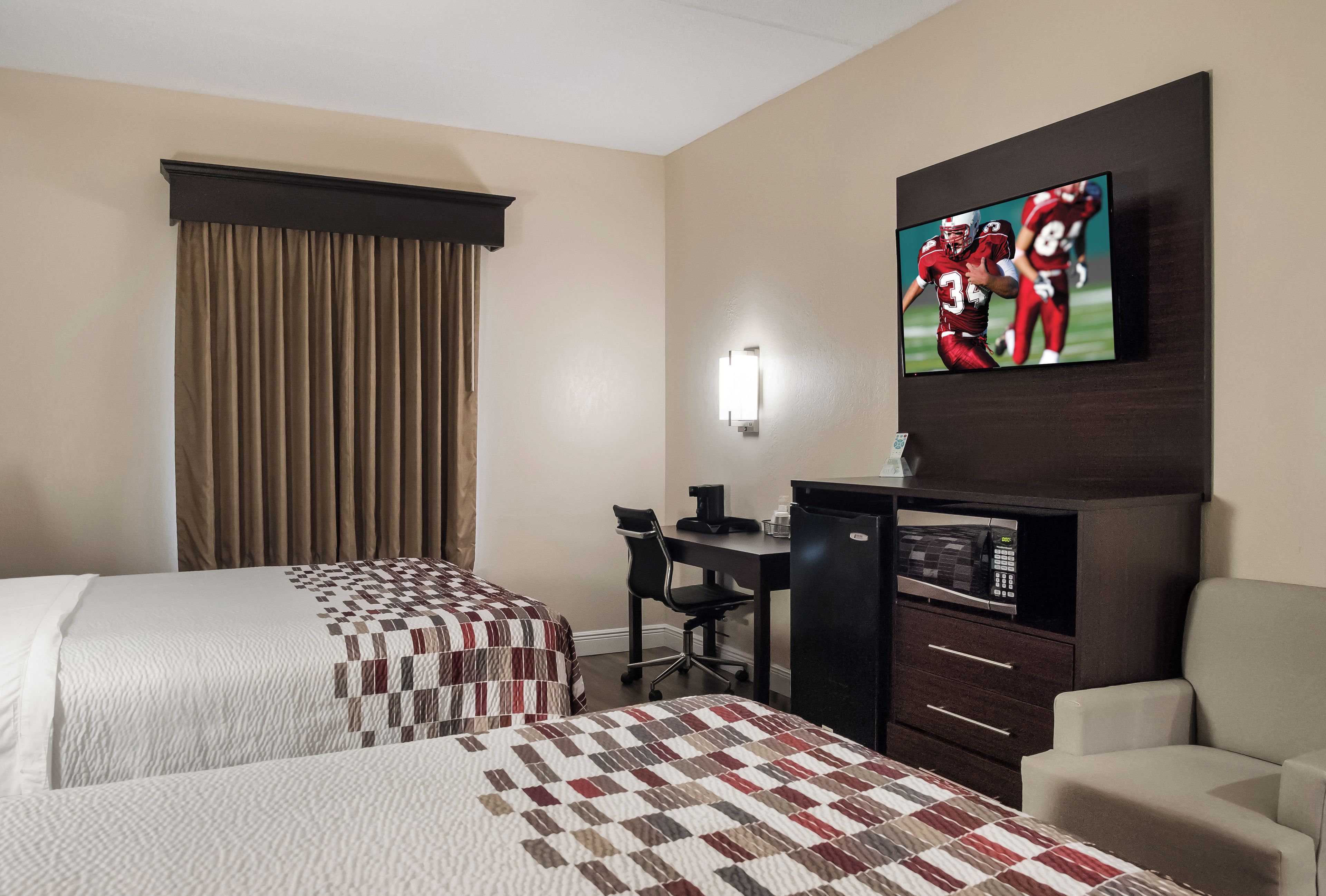 Habitación de hotel con dos camas, un escritorio, una silla, un televisor y un microondas.