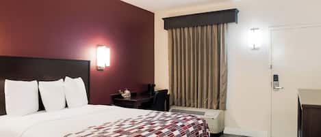 Ein Hotelzimmer mit Bett, Schreibtisch, Stuhl, Kleiderschrank und einem Fenster mit Vorhängen.