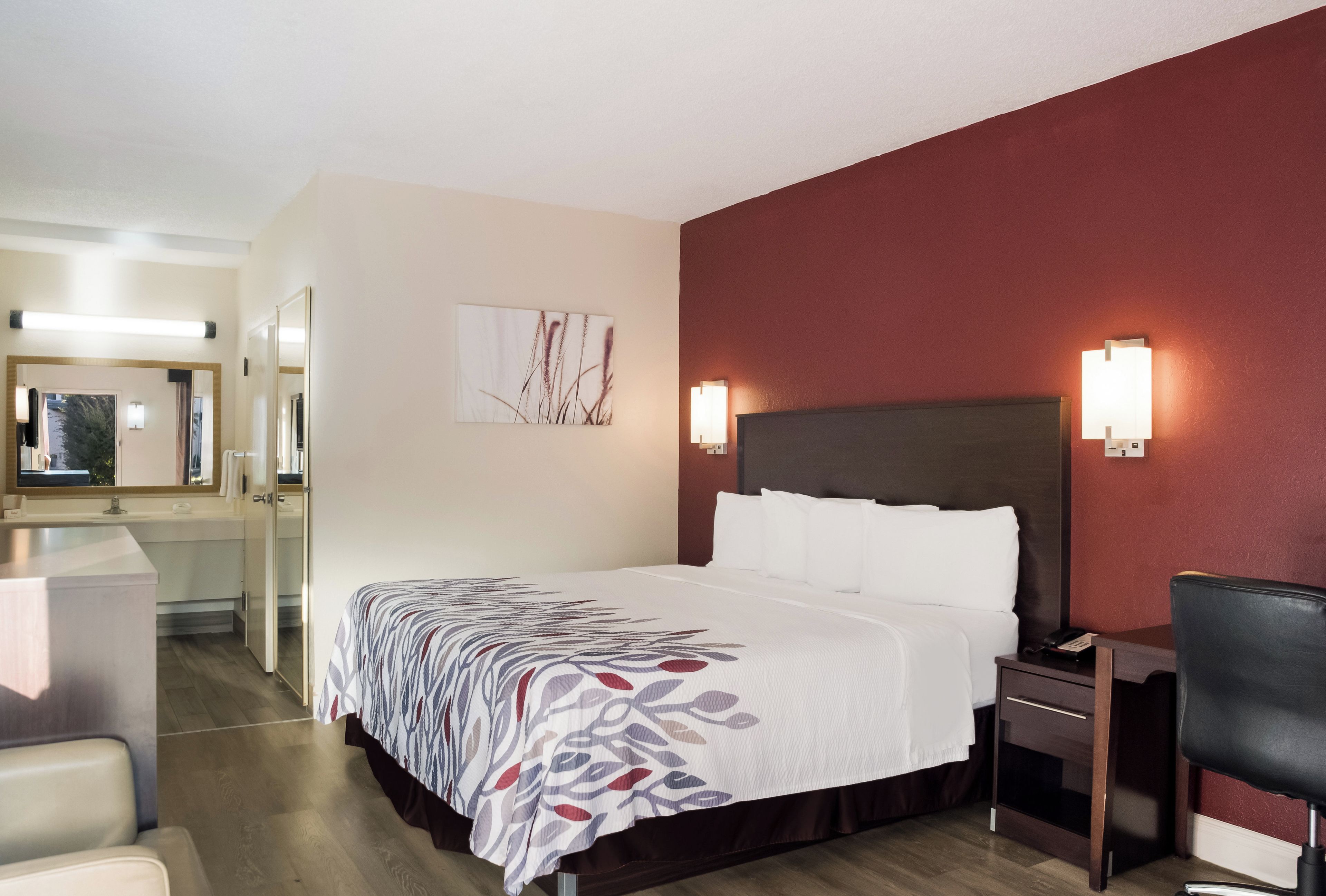 Una habitación de hotel con cama, mesita de noche, silla y espejo.