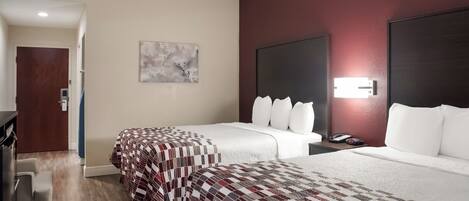 A hotel room with two beds, a desk, a chair, a painting on the wall, and a door leading to another room.