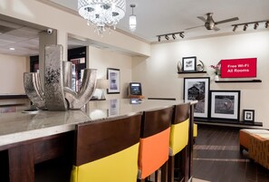 A hotel lobby with a reception desk, a chandelier, framed pictures on the wall, and a sign indicating free Wi-Fi in all rooms. - Red Roof Inn Tupelo (Tupelo)