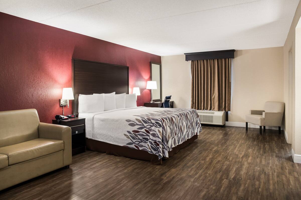 A hotel room with a bed, a desk, a chair, a sofa, and a window with curtains.