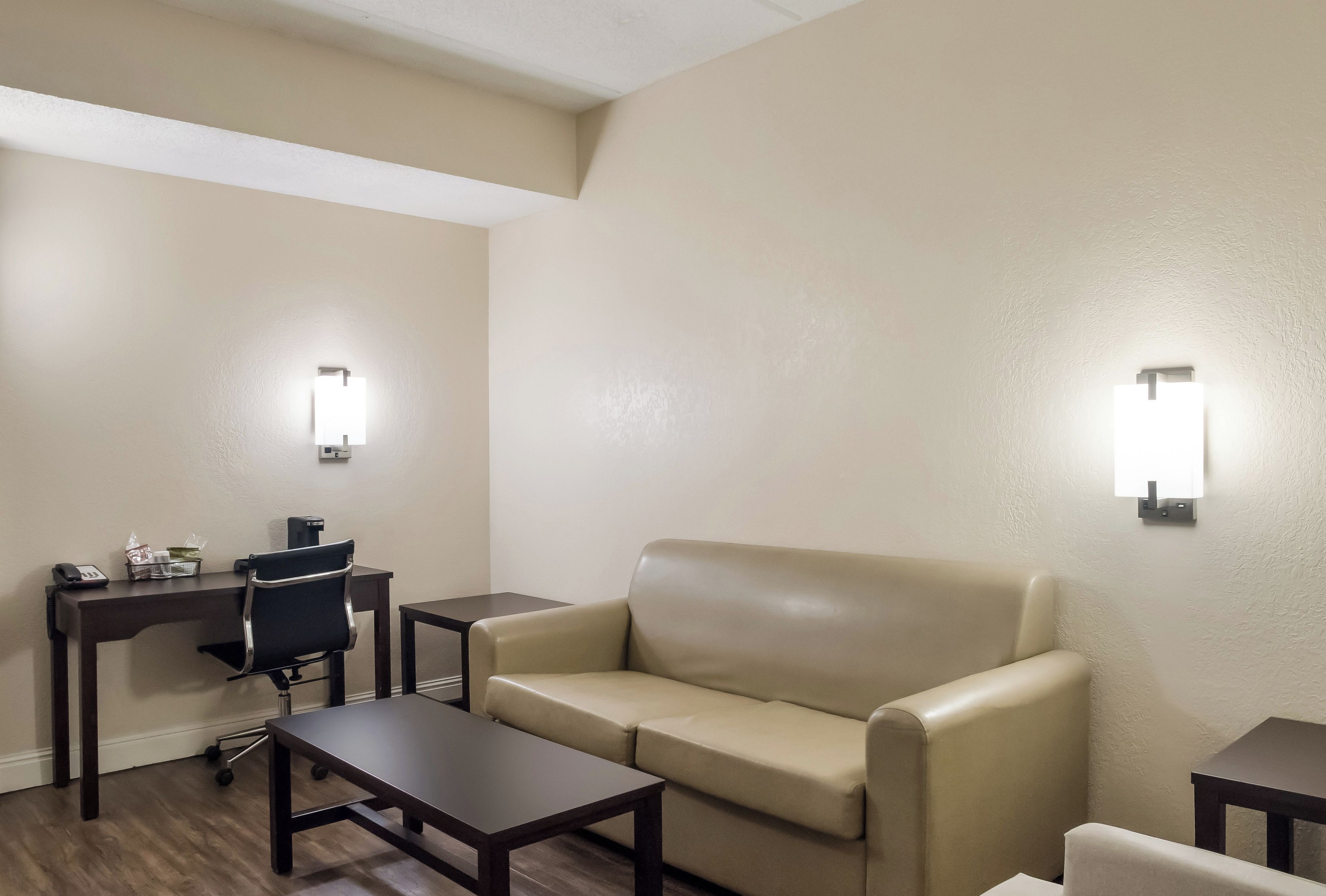 Una habitación de hotel con sofá, escritorio, silla y dos luces fijadas a la pared.