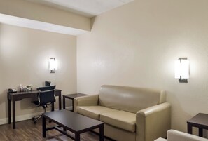 A hotel room with a sofa, a desk, a chair, and two wall-mounted lights. - Red Roof Inn Tupelo (Tupelo)