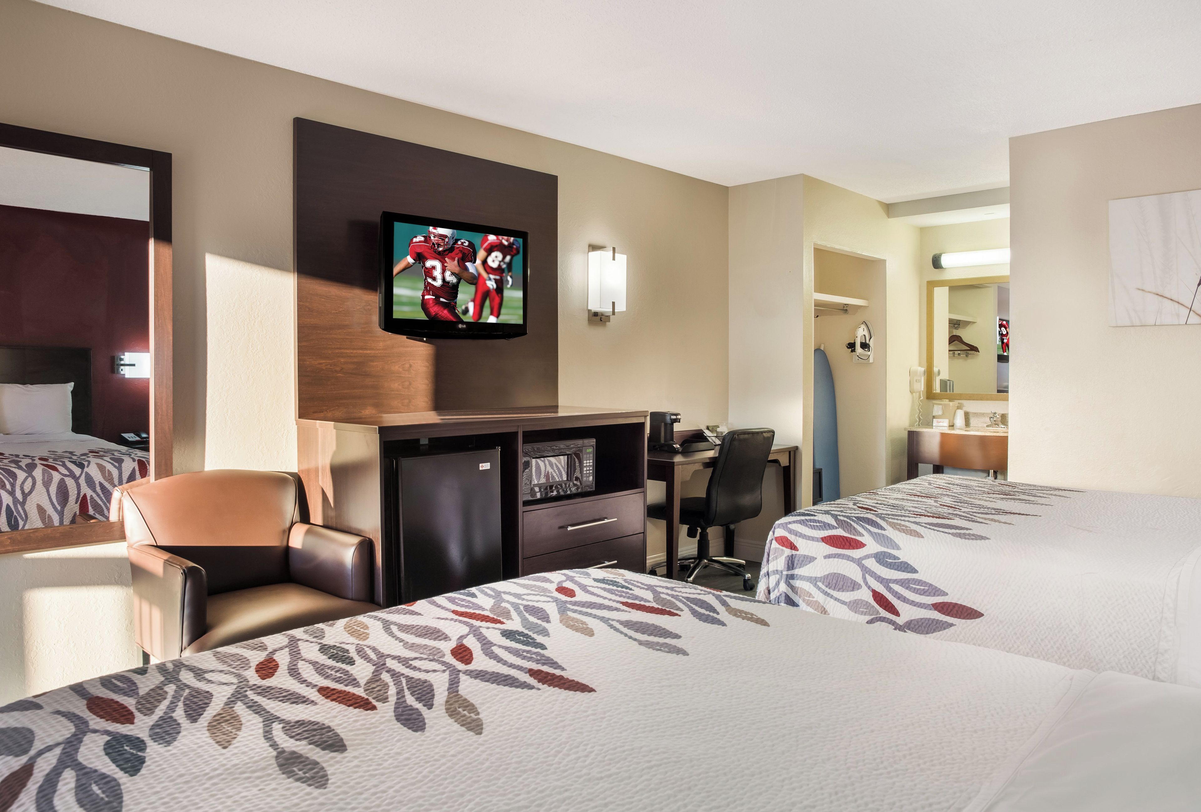 A hotel room with two beds, a desk with a television, a chair, a desk lamp, and a mirror.