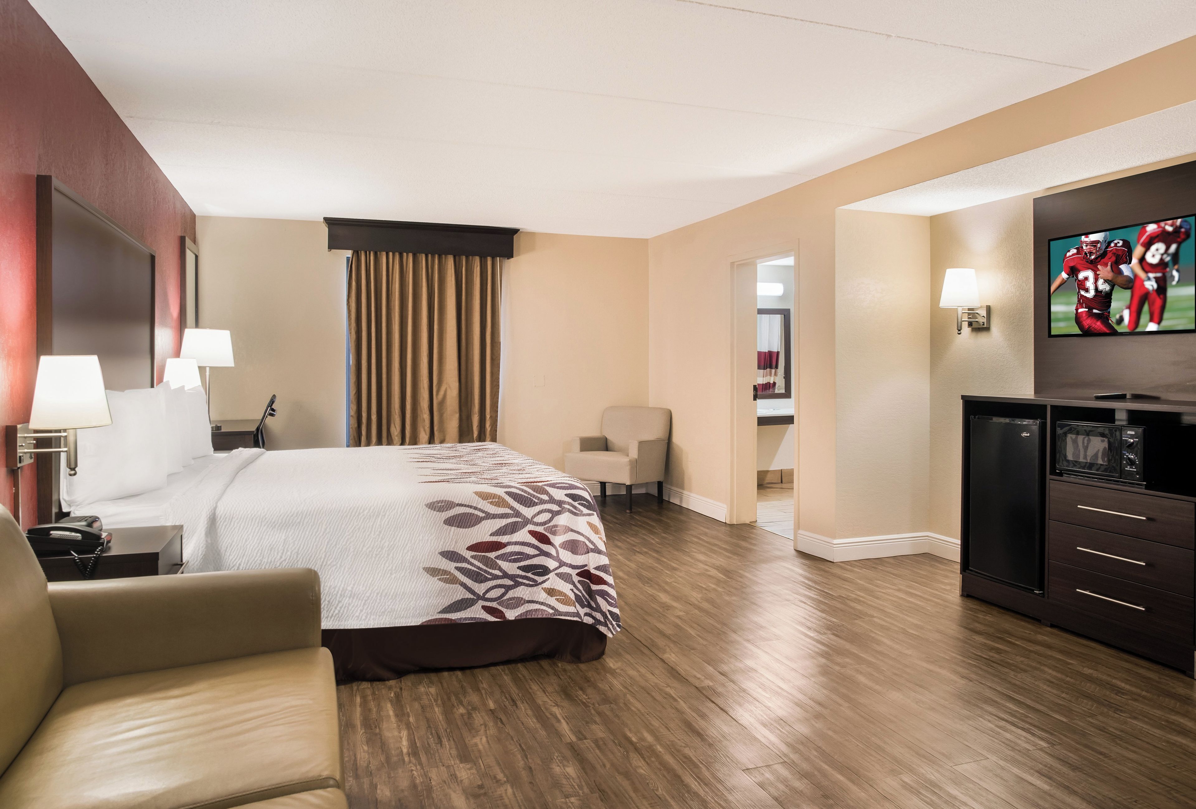 A hotel room with a bed, a desk with a lamp, a chair, a television, and a refrigerator.