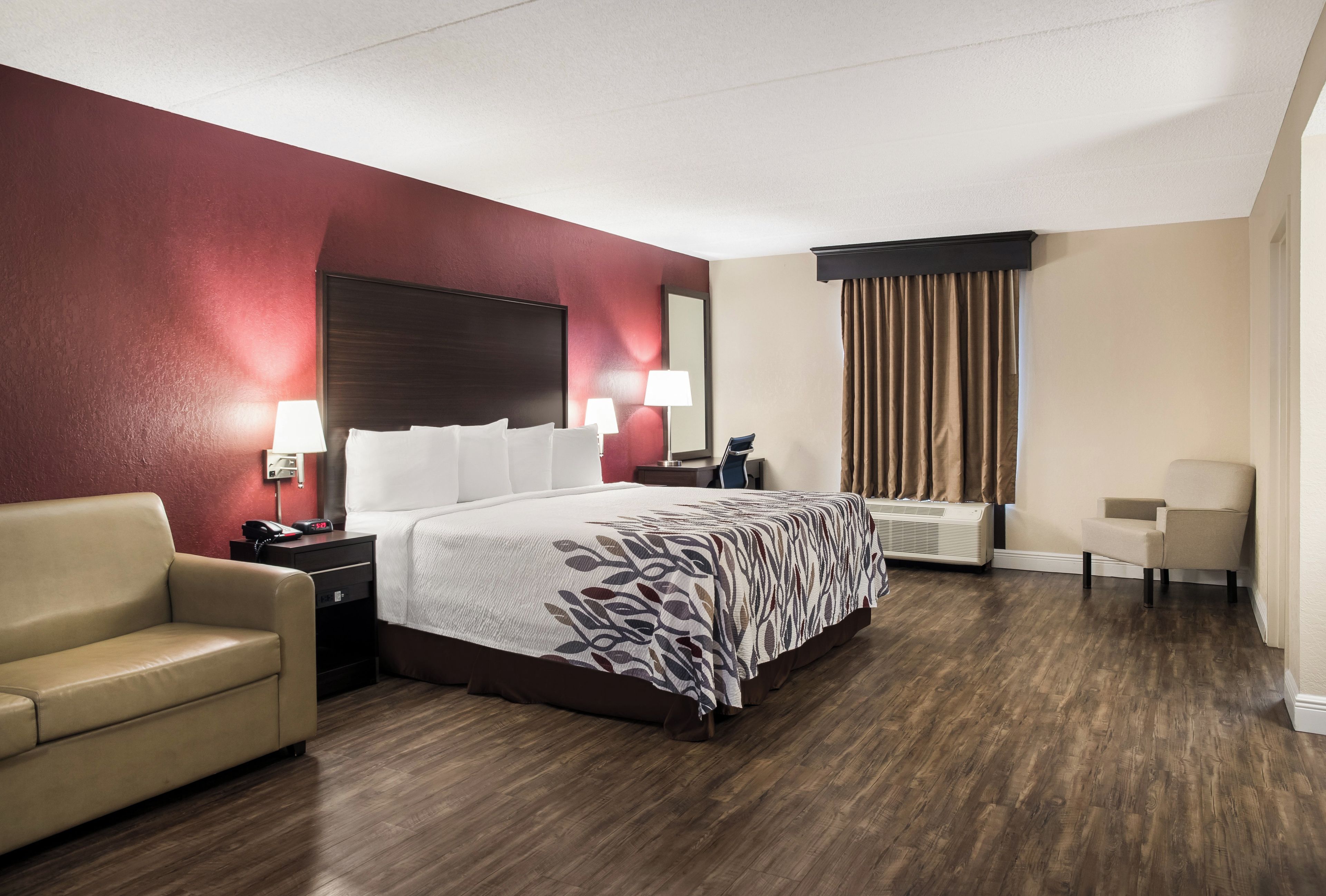 A hotel room with a bed, a desk, a chair, and a sofa.