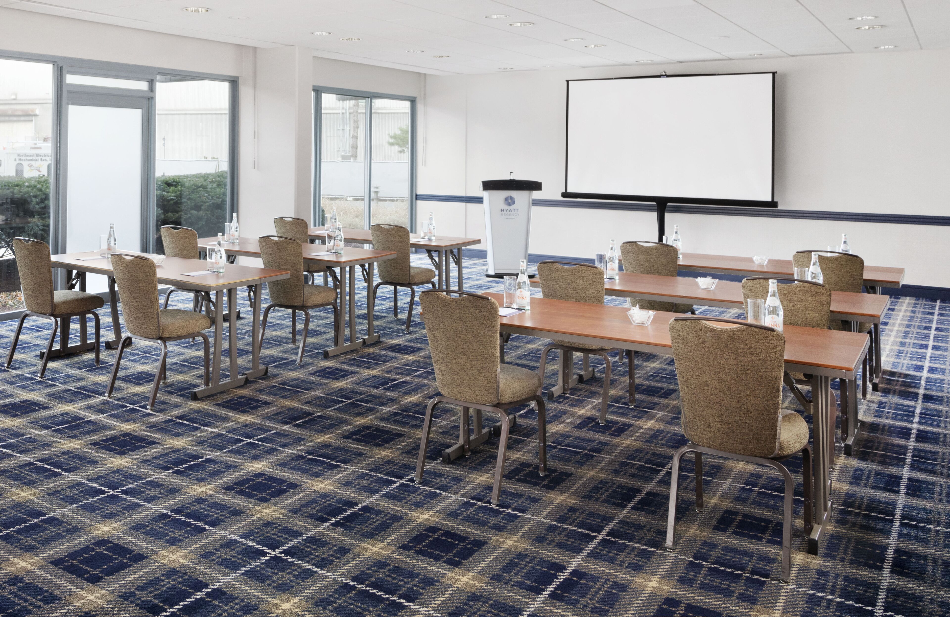 A conference room with a large screen, multiple tables, chairs, and a podium.