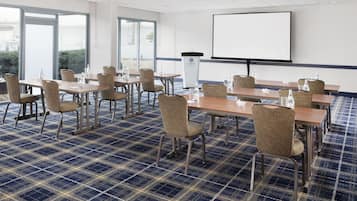 A conference room with a large screen, multiple tables, chairs, and a podium.