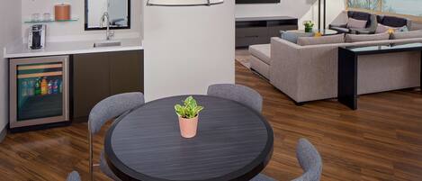 A modern living room with a round dining table, grey sofas, a flat-screen TV, and a city view.