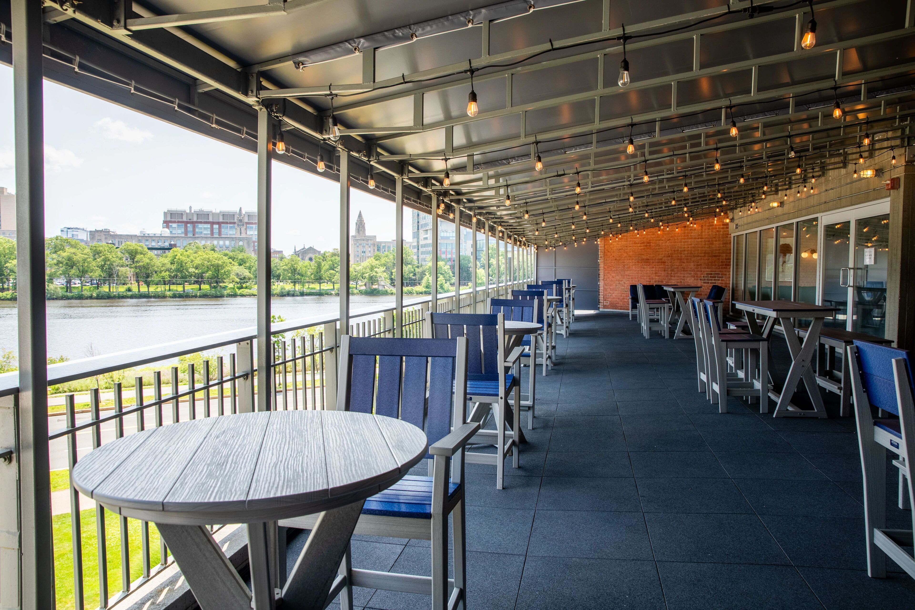 Een terras met tafels en stoelen, met uitzicht op een rivier en stadsbeeld.