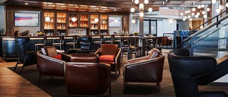 A modern bar area with leather seating, a bar counter with liquor bottles, and a staircase in the background.