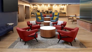 Een moderne lounge met rode en blauwe fauteuils, een houten tafel in het midden en een keuken op de achtergrond.