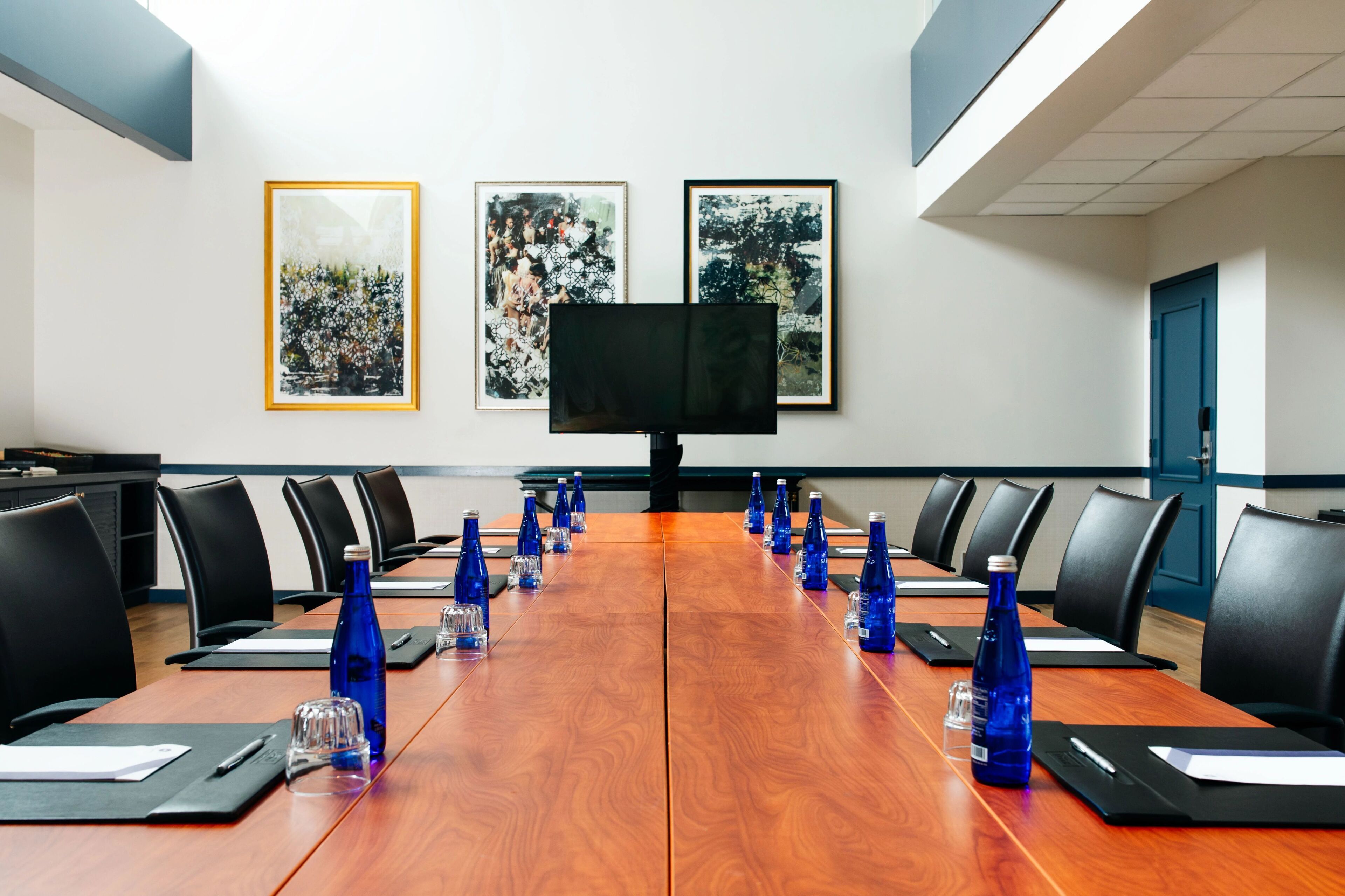 Un salón de conferencias con una larga mesa de madera, sillas negras y botellas de agua azules.