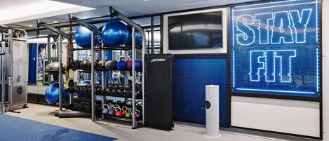 A gym with exercise equipment, a blue mat, and a neon sign that reads "STAY FIT".