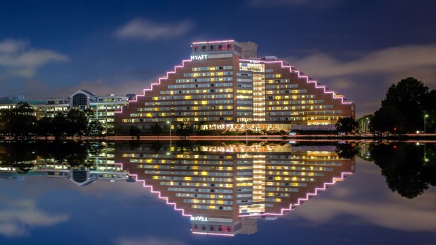 Um hotel de vários andares com um design escalonado característico, com letreiros iluminados e reflexo na água.