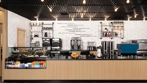 A modern coffee shop interior with a counter displaying pastries, a coffee machine, and a menu board.
