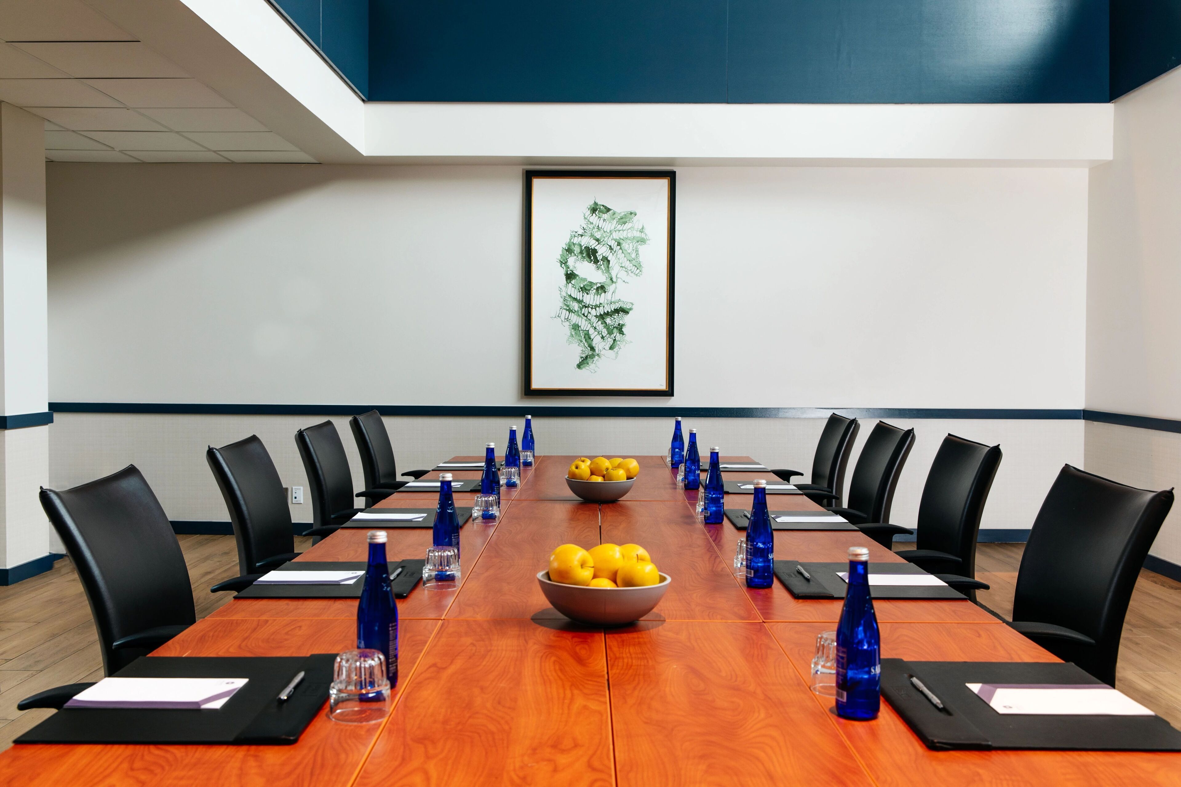 A conference room with a long table, black chairs, and a framed artwork on the wall.