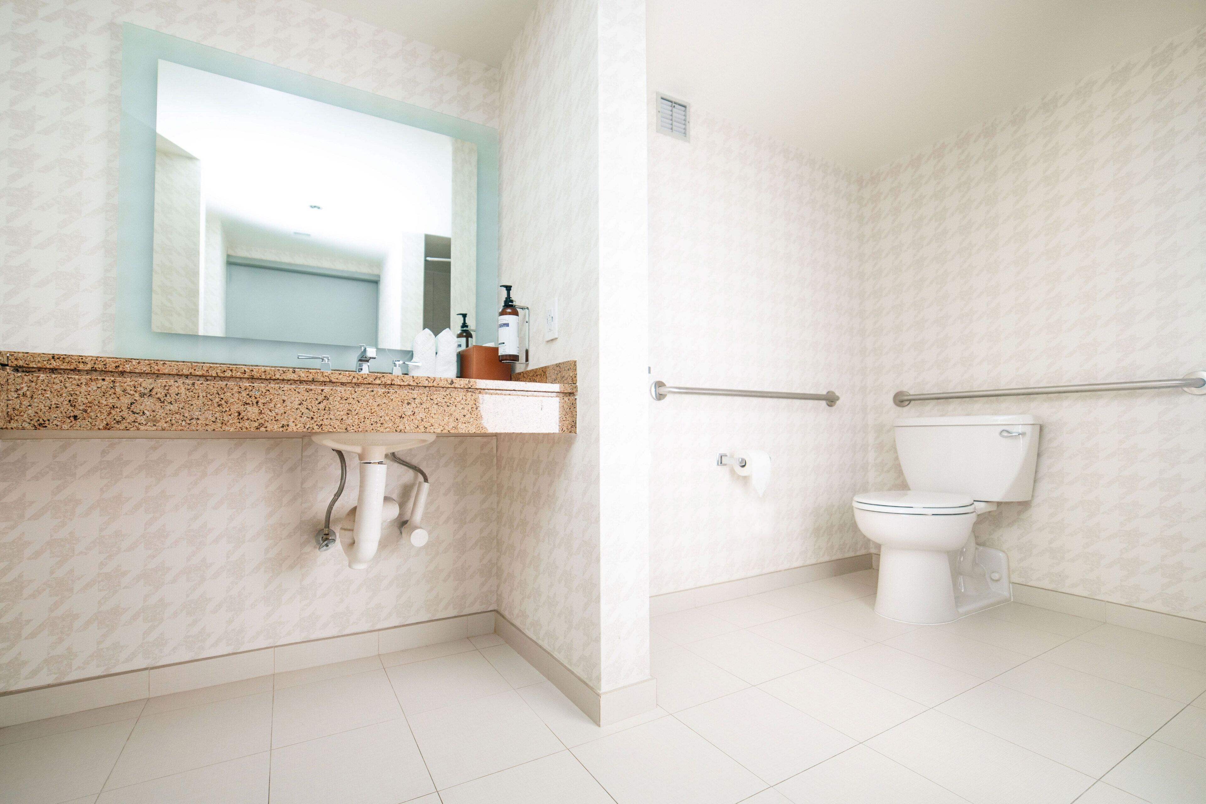 A bathroom with a sink, mirror, toilet, and grab bars.